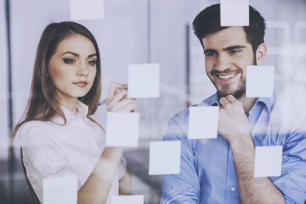 Joven hombre de negocios y mujer de negocios que trabaja en un nuevo proyecto con muchas notas adhesivas en la pantalla de vidrio en la oficina —  Fotos de Stock