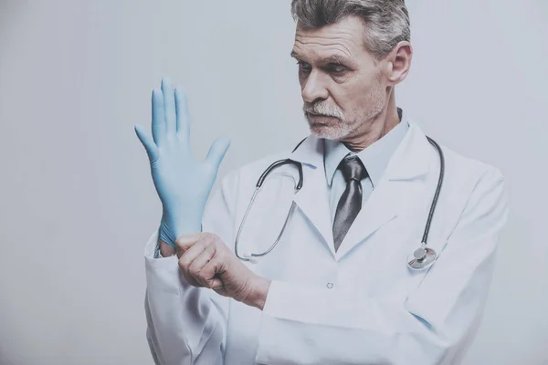 Senior férfi orvos visel kesztyűt, a szürke háttér — Stock Fotó