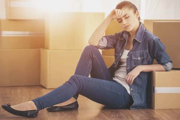A boldog fiatal nő ül egy szobában közelében dobozok. Mozgó, új lakás vásárlása — Stock Fotó