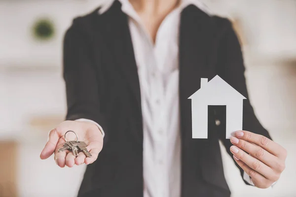 Close-up of hands of realtor woman is holding keys and model of home — Stock Photo, Image