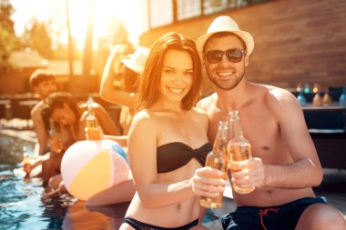 Yakışıklı yaz şapka ve güzel kadın yüzme havuzunda bira şişeleri ile tezahürat.