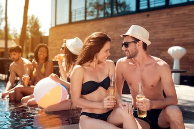 Yakışıklı olan yaz hasır şapkalı kız havuzda otururken mayo ile flört ediyor. Yüzme havuz partisi. Arkadaş şirket yüzme havuzunda eğlenceli yaşıyorsanız.