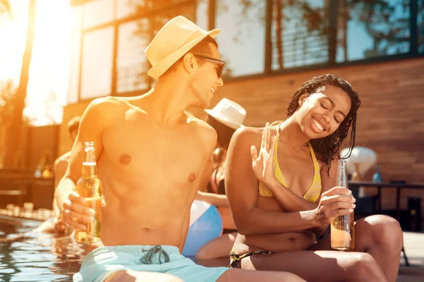 Joven en verano sombrero de paja coquetea con chica en traje de baño que lo evita en la piscina . — Foto de Stock