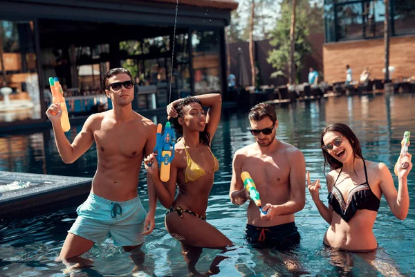 Company of friends with water guns have fun in pool, carefree spending time. Resting on pool. Holidays in swimming pool at aquapark.