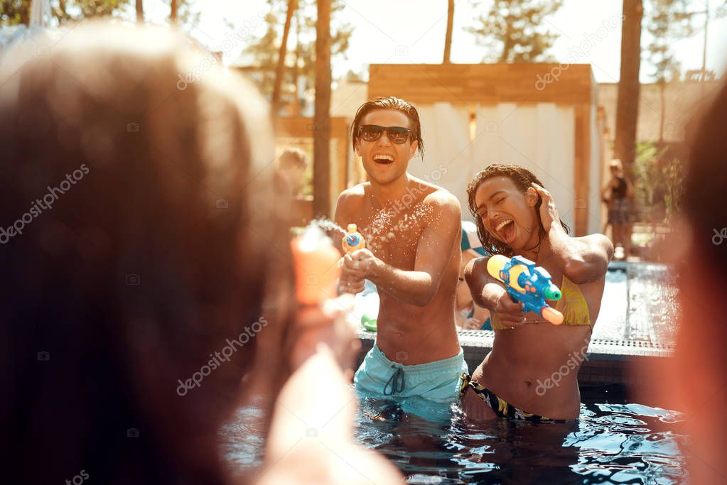 Multiethnic company of friends in swimming pool at summertime. Swimming pool party. Group of people are having fun in swimming pool at summertime.