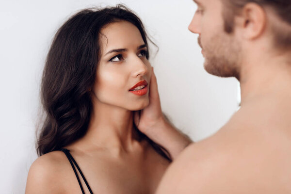 Long-haired man gently strokes cheek of beautiful brunette woman in lingerie. Intimate affinity. Desire and temptation.