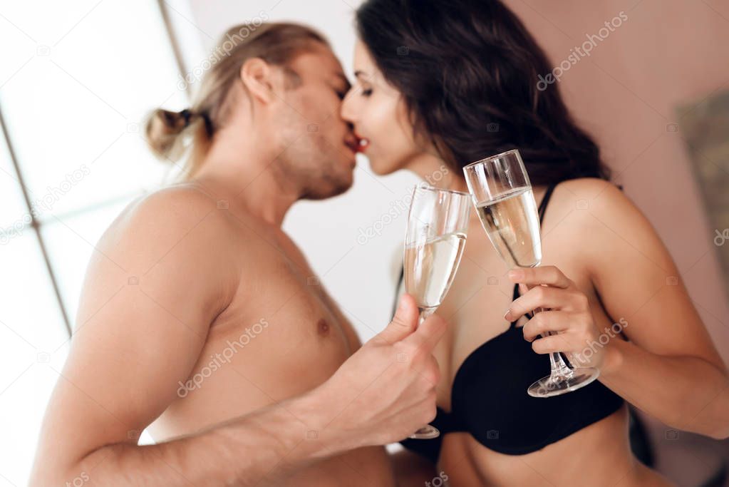 Young passionate couple cheers with glasses of champagne in bed. Romantic encounter. Intimate relationship. Sexual relations.