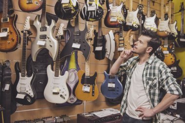 Genç adam elektrik gitar müzik mağazası dikkate alınarak