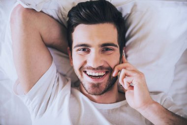 Adam yatak yatak odasında yatan ise telefonla konuşuyor.