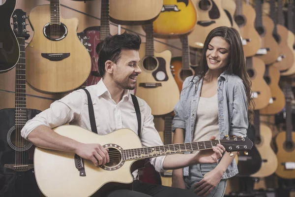 Man is playing guitar near young girl on a background of guitars in the music store — Stock Photo, Image