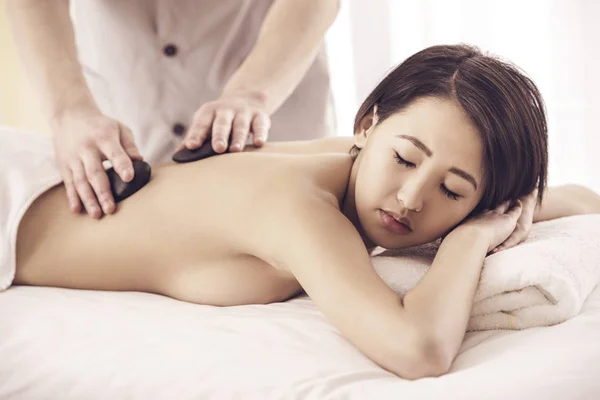 Masajista masculino haciendo masaje en el cuerpo de la mujer con piedras de basalto zen en el salón de spa — Foto de Stock