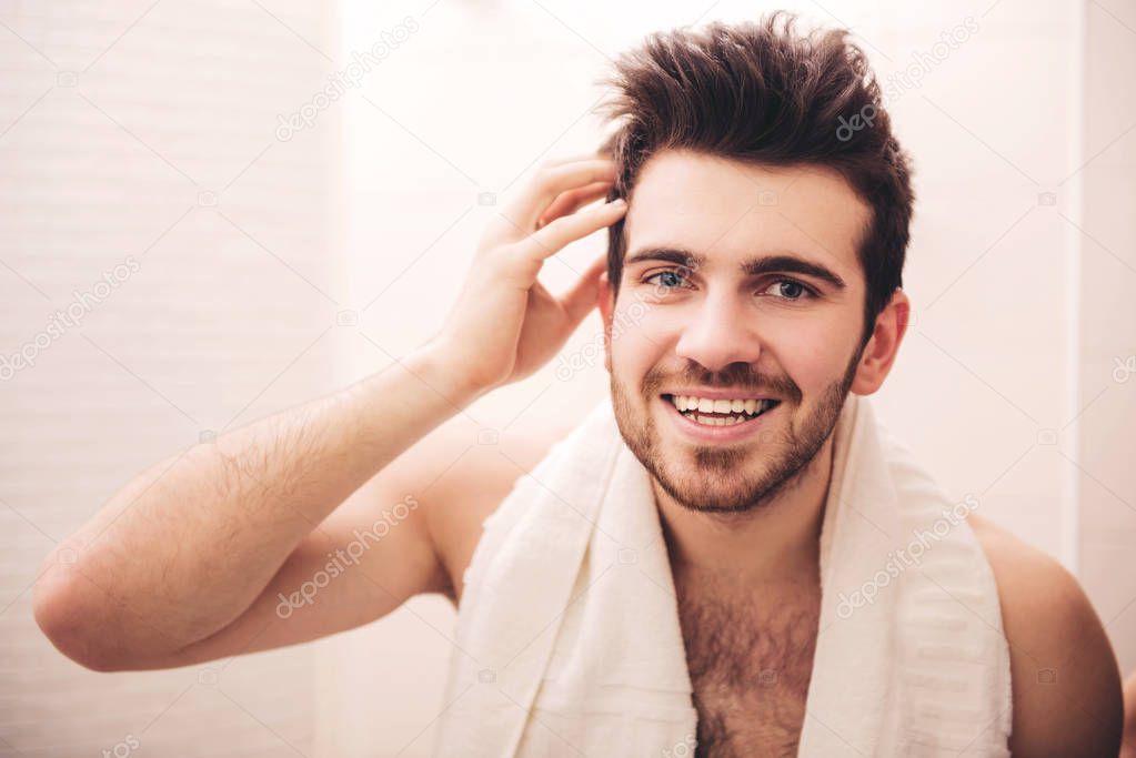 Man is touching his hair, smiling in bathroom in morning.