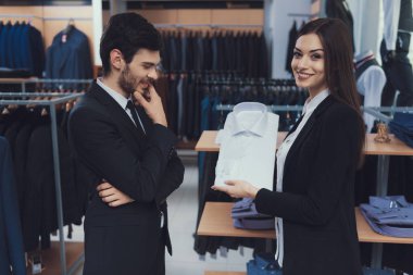 Başarılı genç işadamı görünüyor gömleğe Danışmanı iş tarzı giyim mağazasında gösterir.