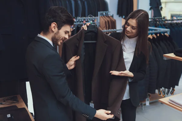 Hermosa chica elegante presenta chaqueta de estilo empresarial a hombre seguro en la tienda de ropa de los hombres . — Foto de Stock