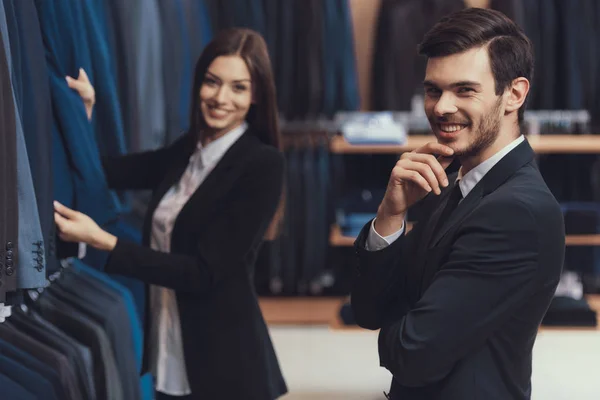 Consultora feminina loja de moda masculina ajuda a escolher jaqueta para homem jovem de terno . — Fotografia de Stock