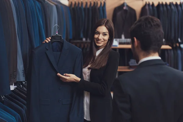 Gyönyörű női férfi ruházat store tanácsadó segít választani a fiatal férfi kabát öltöny. — Stock Fotó