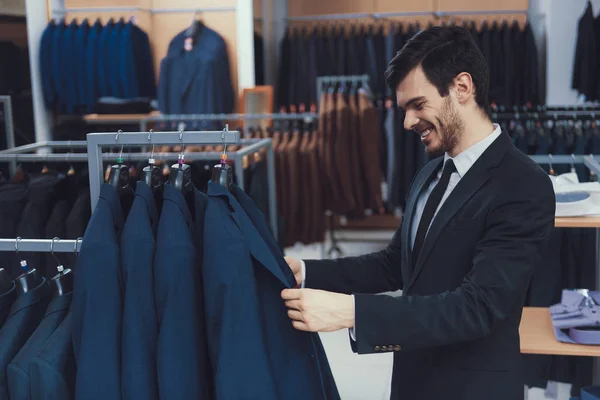 Successful young businessman looks at jacket in business mens clothing store. — Stock Photo, Image