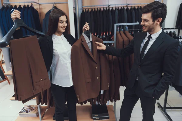 Mooi elegant meisje presenteert zakelijke stijl jas tot zelfverzekerde man bij mannen kleding winkel. — Stockfoto
