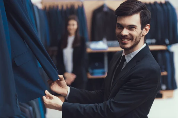 Sourire jeune homme réussi vérifie la qualité du tissu de veste dans le magasin de vêtements pour hommes . — Photo