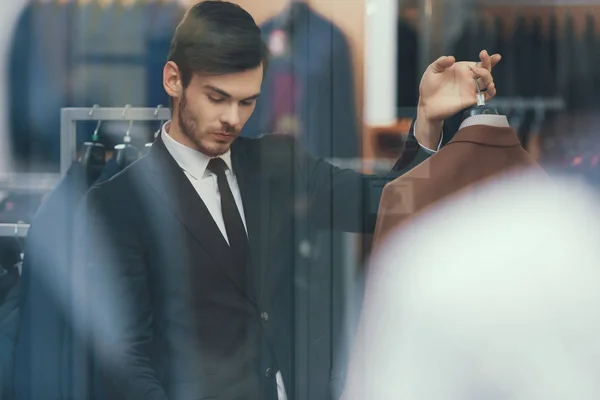 Exitoso joven empresario mira la chaqueta en la tienda de ropa para hombres de negocios . — Foto de Stock