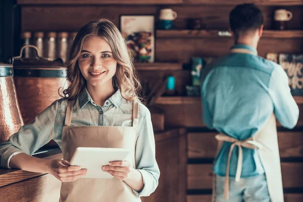 Portret van mooie barista in schort met tablet in café. — Stockfoto