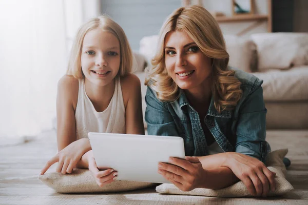 Mature blond woman with cute daughter watching tablet while lying on floor. — Stock Photo, Image