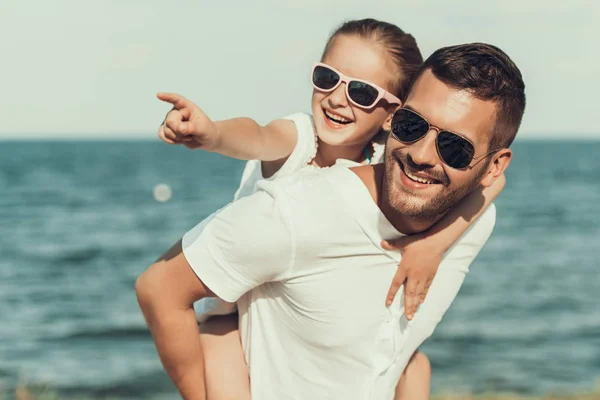 Feliz hijita en gafas de sol se sienta en los padres espalda . — Foto de Stock