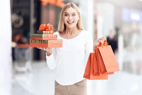 Счастливая блондинка с сумками и подарочными коробками в торговом центре . — стоковое фото