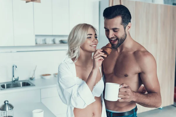 Casal feliz está comendo croissants com café na cozinha . — Fotografia de Stock