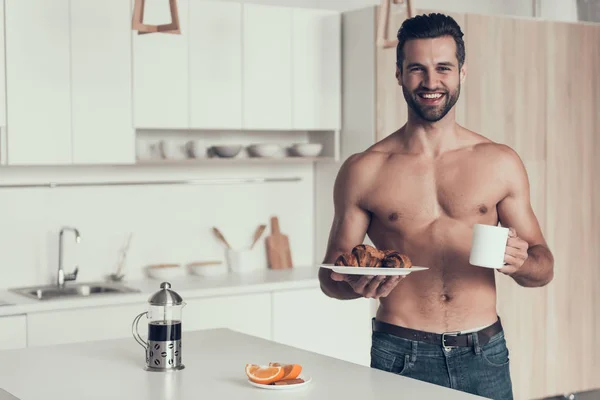 Knappe man met naakte torso gekookte verse koffie en croissant. — Stockfoto