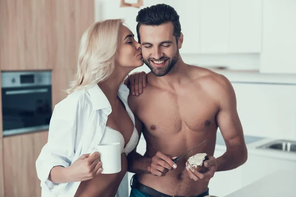 Beautiful wife in negligee with cup of coffee kisses husband. — Stock Photo, Image