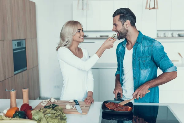 Hustru gör sallad, medan make frites kött i köket. — Stockfoto