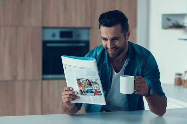 Przystojny mężczyzna pije kawę i czyta prasy w kuchni. — Zdjęcie stockowe
