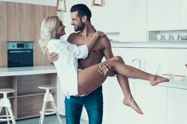 Handsome, brawny man is holding woman on arms at kitchen. — Stock Photo, Image