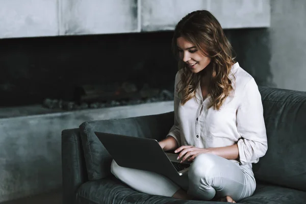 Young woman is typing request on laptop sitting by fireplace.