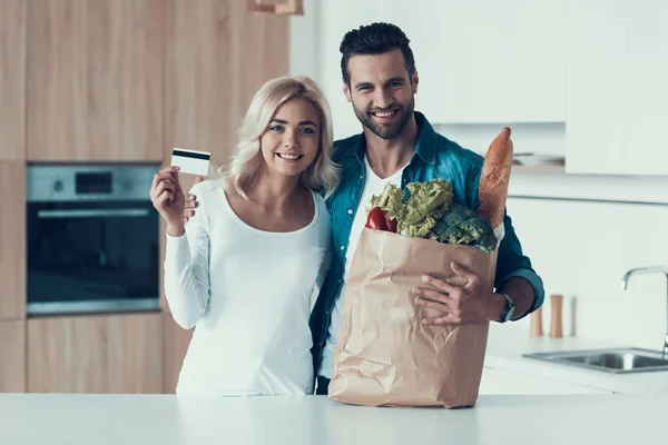 Volwassen gelukkige paar staat in de keuken met pakket van producten. — Stockfoto