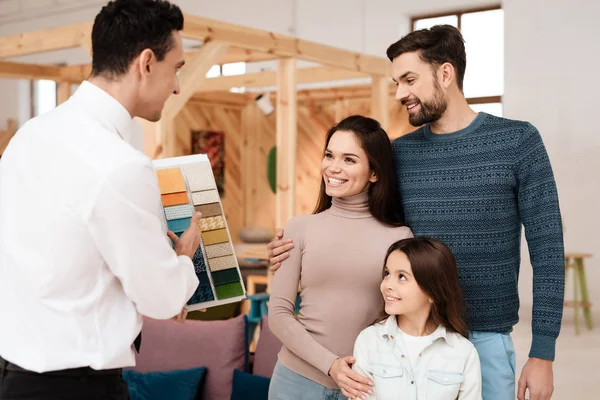 The manager of the furniture store holds samples of fabrics for furniture upholstery. Near him are a mom, dad and the girl. They are furniture buyers.