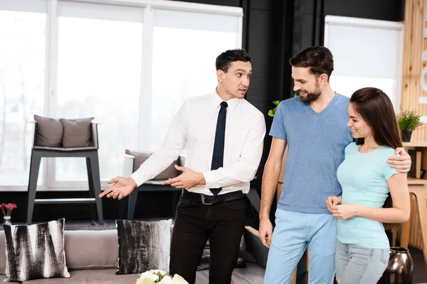 The furniture store manager demonstrates furniture to the buyers. A guy and a girl are listening with a good mood to the seller.