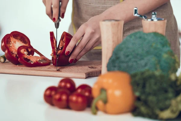 Weibliche Hände schneiden Paprika auf Holzbrett. — Stockfoto