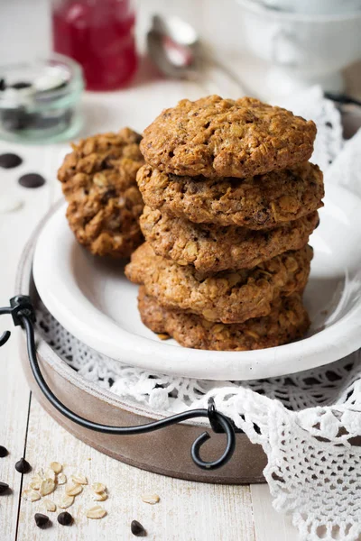 Stack of oatmeal cookies with chocolate on a light background with flakes and a bottle of milk. — Stock Photo, Image
