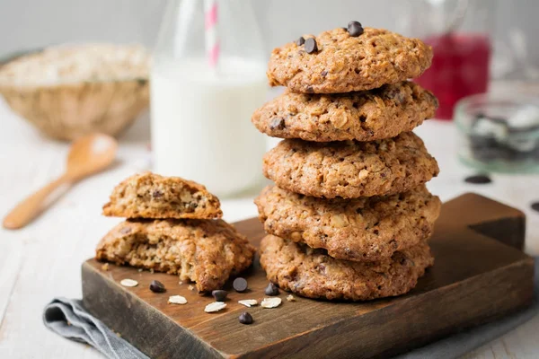 Stack of oatmeal cookies with chocolate on a light background with flakes and a bottle of milk. — Stock Photo, Image