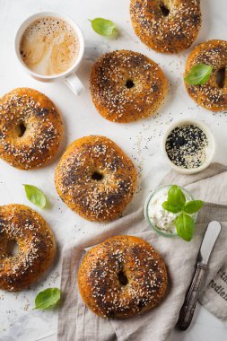 Çeşitli taze tahıllı simit haşhaş tohumu, susam ve hafif beton zemin üzerine kahvaltı için malzemeler.