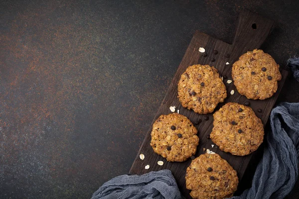 Stos ciasteczka owsiane z czekoladą i płatki na beton ciemny zardzewiałe lub kamienne podłoże. — Zdjęcie stockowe