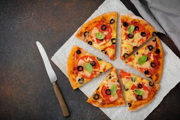 Pizza margarita with tomatoes, mazarella and slices of olives on a dark concrete or stone background.
