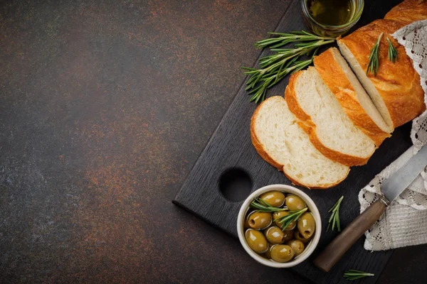 Traditionelles italienisches Ciabatta-Brot mit Oliven, Olivenöl, Pfeffer und Rosmarin auf dunklem Stein- oder Betongrund. — Stockfoto