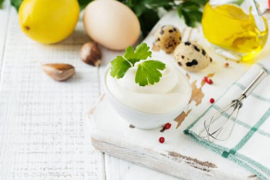 Beyaz seramik kasede geleneksel mayonez sosu ve beyaz ahşap arka planda hazırlanması için malzemeler. Seçici odak.