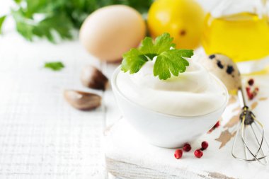 Beyaz seramik kasede geleneksel mayonez sosu ve beyaz ahşap arka planda hazırlanması için malzemeler. Seçici odak.