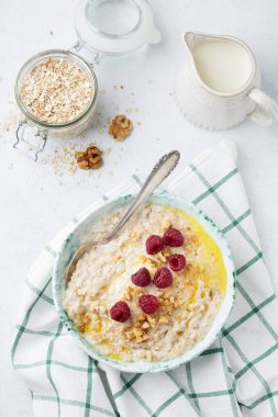 Taze ahududu, ceviz ve bir ışık taş veya beton arka plan bir seramik tabak tereyağı ile yulaf lapası. Seçici odak.