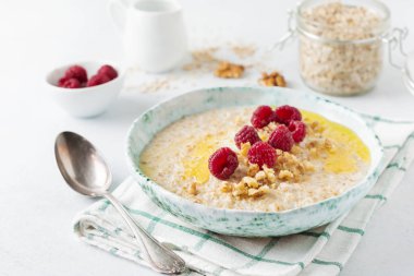 Taze ahududu, ceviz ve bir ışık taş veya beton arka plan bir seramik tabak tereyağı ile yulaf lapası. Seçici odak.