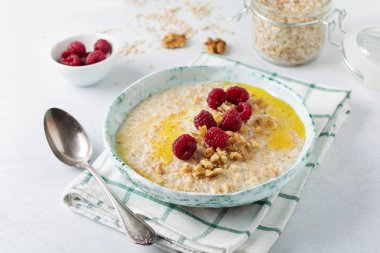 Taze ahududu, ceviz ve bir ışık taş veya beton arka plan bir seramik tabak tereyağı ile yulaf lapası. Seçici odak.